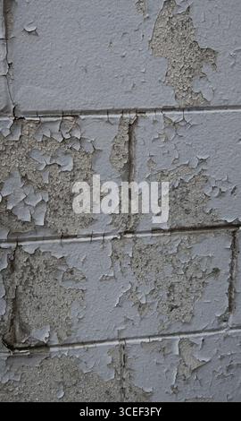 background texture of peeling paint on cement rectangular block wall white paint peeling off to reveal the layer underneath old weathered needs repair Stock Photo