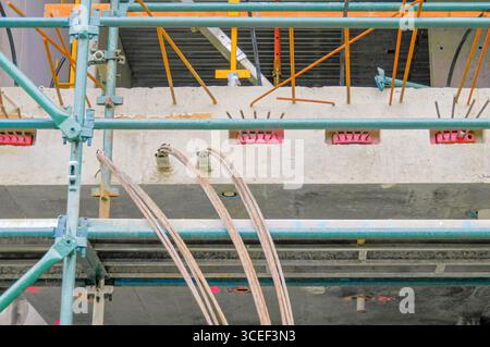 Scaffolding surrounds a concrete slab with protruding cables and metal reinforcement rods, showing construction work in progress Stock Photo