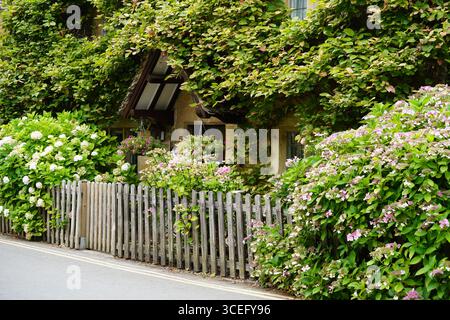 Charming Rustic House Surrounded By Blooming Garden And Wooden Fence. Bourton-on-the-Water, England Stock Photo