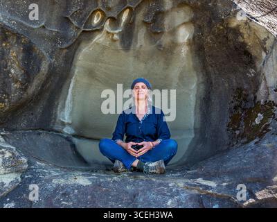 Young woman meditating in shallow hollow on rock face - Hornby Island, British Columbia, Canada. Stock Photo