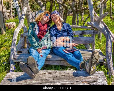 Two women friends sitting and smiling on a hand-built driftwood seat on Hornby Island, British Columbia, Canada. Stock Photo