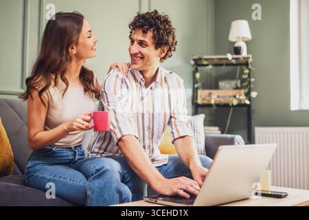 Couple discussing home finance on laptop and calculating family budget in living room. Stock Photo