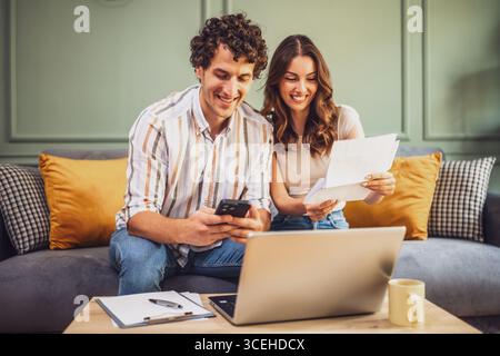 Couple discussing home finance while checking bills. They are checking financial documents and calculating family budget in living room. Stock Photo