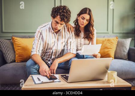 Couple discussing home finance while checking bills. They are checking financial documents and calculating family budget in living room. Stock Photo