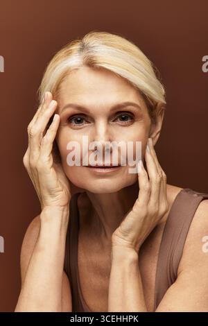A beautiful senior woman gently touching her face, radiating elegance and grace in soft lighting. Stock Photo
