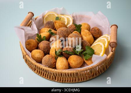 A woven basket filled with assorted Brazilian fried appetizers like Coxinha and cheese balls, garnished with fresh parsley and lemon slices Stock Photo