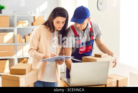 Man from delivery service working in warehouse with female small business owner in logistics center Stock Photo