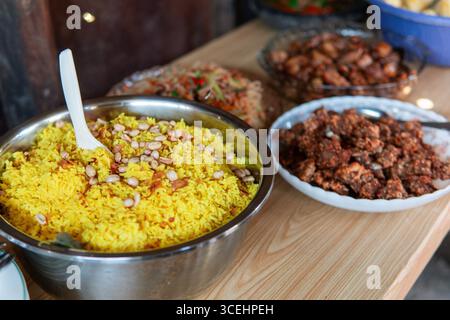 A traditional Indonesian meal featuring yellow rice topped with peanuts and fried shallots, served with assorted side dishes on a wooden table. Stock Photo