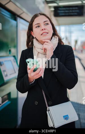 Contemplative female passenger using her cellphone to browse and interact with a mobile app at a transportation station, effectively planning her Stock Photo