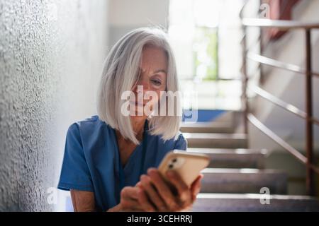 Tired nurse taking break during hospital shift, texting with family. Stock Photo