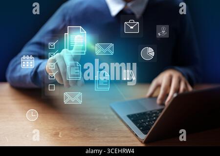 Digital workspace with a person interacting with virtual icons and using a laptop in a modern setting at evening Stock Photo