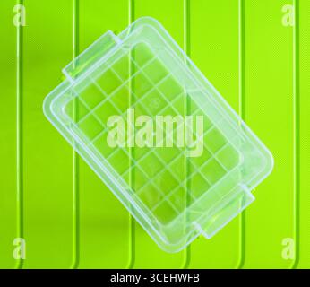 Empty transparent plastic food container resting on a vibrant green surface, enhancing the fresh and simple aesthetic of kitchen organization Stock Photo
