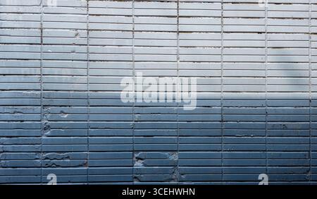 Gradient effect created by blue and gray rectangular tiles covering a wall, showing signs of wear and tear, perfect as a background or texture Stock Photo