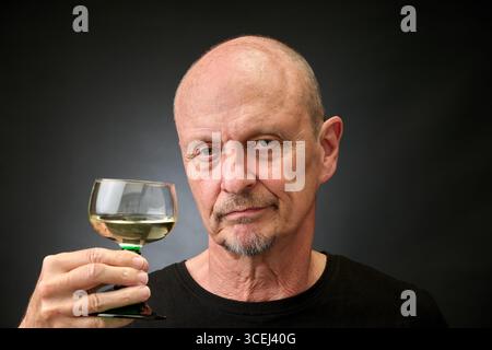 Closeup portrait of a senior man tasting a good white wine in a vintage Harcourt style lighting Stock Photo