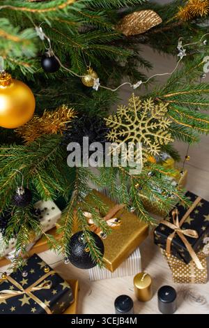 Luxurious gold and black gift boxes arranged beneath a Christmas tree, illuminated by glowing candles , adorned with elegant decorations, creating a c Stock Photo