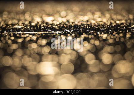 Abstract blurry golden bokeh reflecting on dark water surface creating a beautiful background Stock Photo