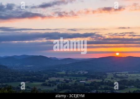 Stunning sunset casting golden light over a picturesque valley nestled amidst rolling mountains Stock Photo