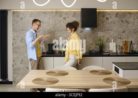 The husband explains his ideas to the young wife actively gesturing his hands during a conversation in the kitchen Stock Photo