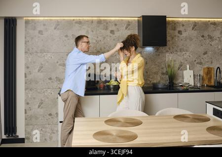 Couple enjoying a playful moment in a modern kitchen while preparing a meal together Stock Photo