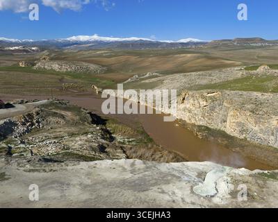 Brown river flows through rugged rocks in a vast landscape under a clear blue sky, aerial view, Diyadin, Murat River, thermal spring, Agri Province, A Stock Photo