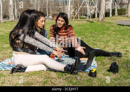 Three students collaborating on a project outdoors, using a laptop and portable speaker Stock Photo