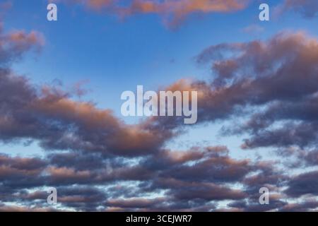 Layered clouds at dusk glowing with soft orange light against a deep blue sky Stock Photo