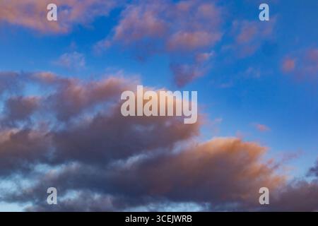 Dramatic clouds at sunset with soft orange light against a vivid blue sky Stock Photo