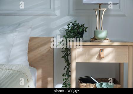 Bedside table with lamp and other decor near bed indoors Stock Photo