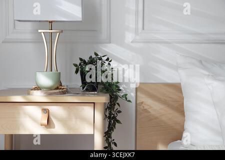 Bedside table with lamp and other decor near bed indoors Stock Photo