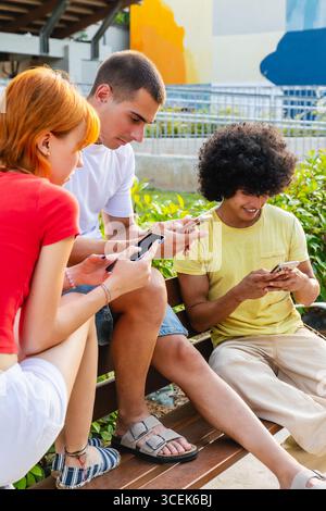 Young students using smartphones sitting on bench outdoors Stock Photo