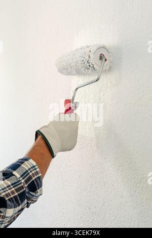Close-up of hand wearing protective gloves. A painter paints a masonry wall with white paint using a roller. Construction industry. Safety at Work. Stock Photo