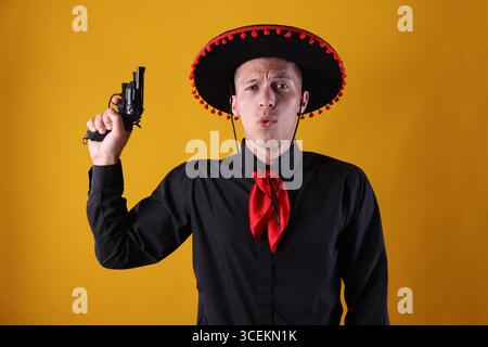 Man in black Flamenco hat with gun on yellow background Stock Photo