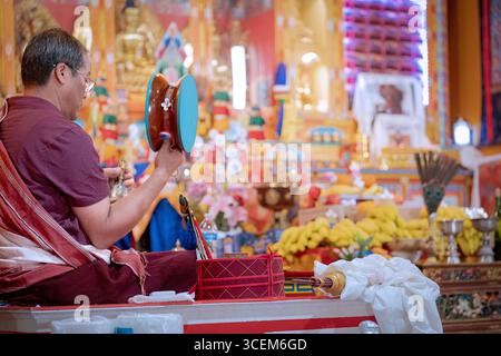 A Buddhist monk leads a puja service in a temple while ringing a bell & rotating a damaru drum. In Elmhurst, Queens, New York City. Stock Photo