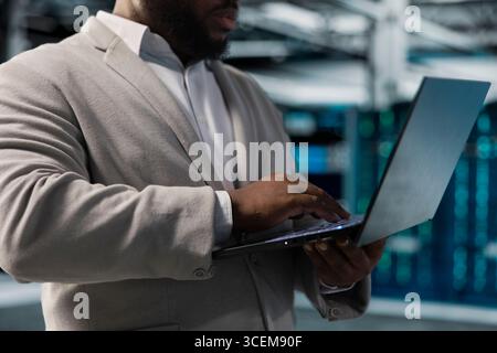 Close up of server hub worker running maintenance scans, fixing network issues affecting rigs performance. Data center admin running system diagnostic tests on laptop, tracking resource utilization Stock Photo