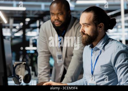 Team of technicians in data center using PC to update storage arrays software, configuring network virtualization. Teamworking colleagues in server room using computer to verify settings Stock Photo