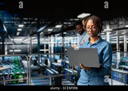Data center female system administrator performing maintenance with AI for automation. Engineering specialist managing data infrastructure used for machine learning in server hub. Stock Photo