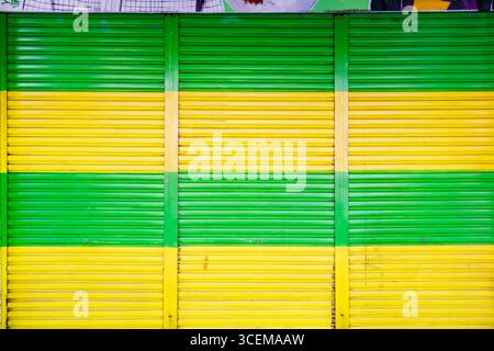 Colorful abstract storefront with alternating green and yellow horizontal stripes metal shutters vibrant geometric pattern George town Penang Malaysia Stock Photo
