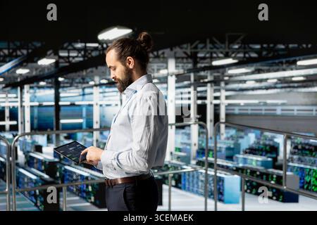 General manager manages code programming with tablet on industrial platform, handling software updates for server rigs and AI configuration. Male IT expert ensuring data management. Stock Photo