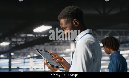Data center programmer checking lines of code and colleague reviewing AI LLM visualizations. IT experts analyze neural networks outputs to ensure stable infrastructure operations, using tablet Stock Photo