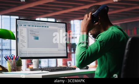 Tech savvy black engineer developing secure online program at home. Surrounded by binary data, freelancer works on interface design, script optimizations and network systems. Camera A. Stock Photo
