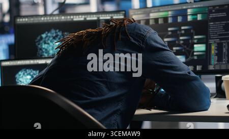 Irritated data center engineer punching desk, irked by glitches while using algorithms to analyze datasets. Mad server hub developer raging, annoyed by malfunctioning AI neural networks, camera B Stock Photo