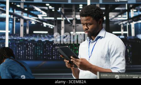 Data center engineer using tablet to interpret AI generated data analytics graphs. Server room worker using artificial intelligence displaying system performance predictive metrics, camera B Stock Photo