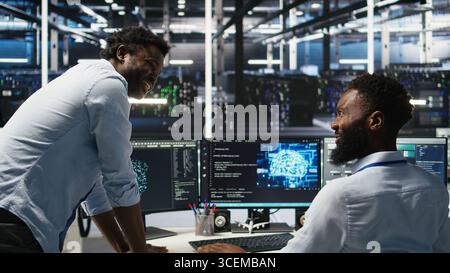Pleased data center manager praising work done by engineer using neural network models to configure hardware. Supervisor congratulating employee for successfully using AI to optimize system, camera A Stock Photo