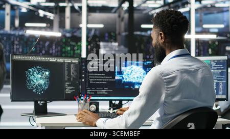Manager supervising data center engineer using AI neural network models to configure hardware. Team leader overseeing employee using machine learning programming language to optimize systems, camera B Stock Photo