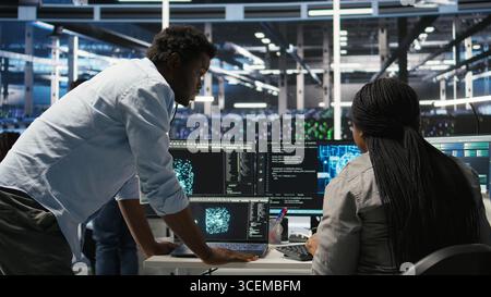 Data center engineering team uses artificial intelligence deep learning models to configure gear. Teamworking colleagues work on AI programming language in server farm, optimizing system, camera A Stock Photo