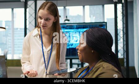 Manager teaching young technician how to develop software and optimize code using AI. Team leader guiding intern in office on how to use artificial intelligence to resolve bottlenecks, camera A Stock Photo