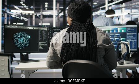 Data center admin does neural networks node tree programming, optimizing resource allocation. Server room IT professional uses predictive deep learning AI visualization systems, camera A Stock Photo