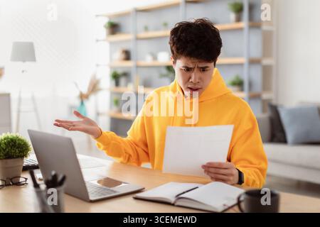 Confused asian man holding paper reading report working on laptop Stock Photo