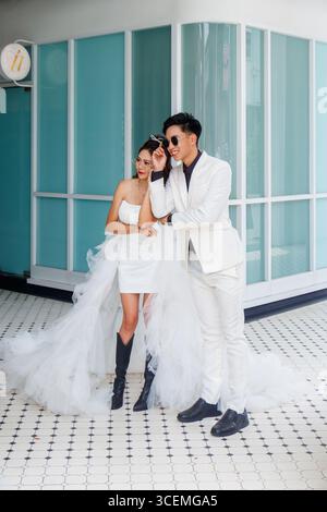 Stylish wedding couple in elegant white outfits with matching sunglasses posing confidently for photographer in George town, penang island malaysia Stock Photo