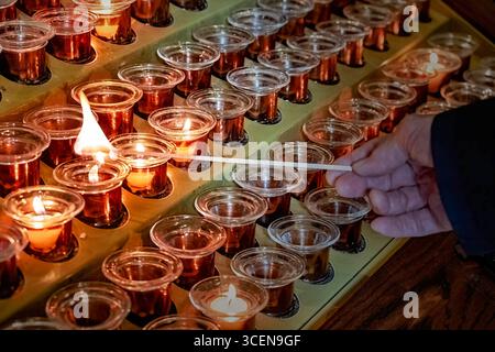 Candles burning in a church with hand visible lighting a candle, symbolizing prayer, hope and memory, warm glow of the flame and the atmosphere of pra Stock Photo